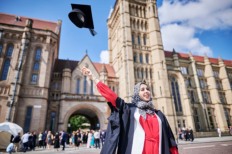 A graduating student throwing her cap in the air in front of Whitworth Hall.