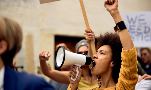 Young African American woman with raised fist shouting through megaphone while being on anti-racism 