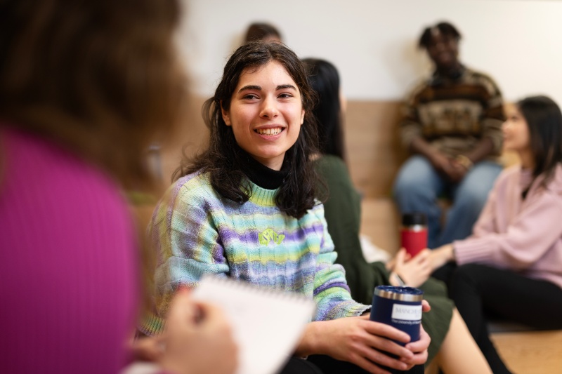 A student smiling while talking to another student.